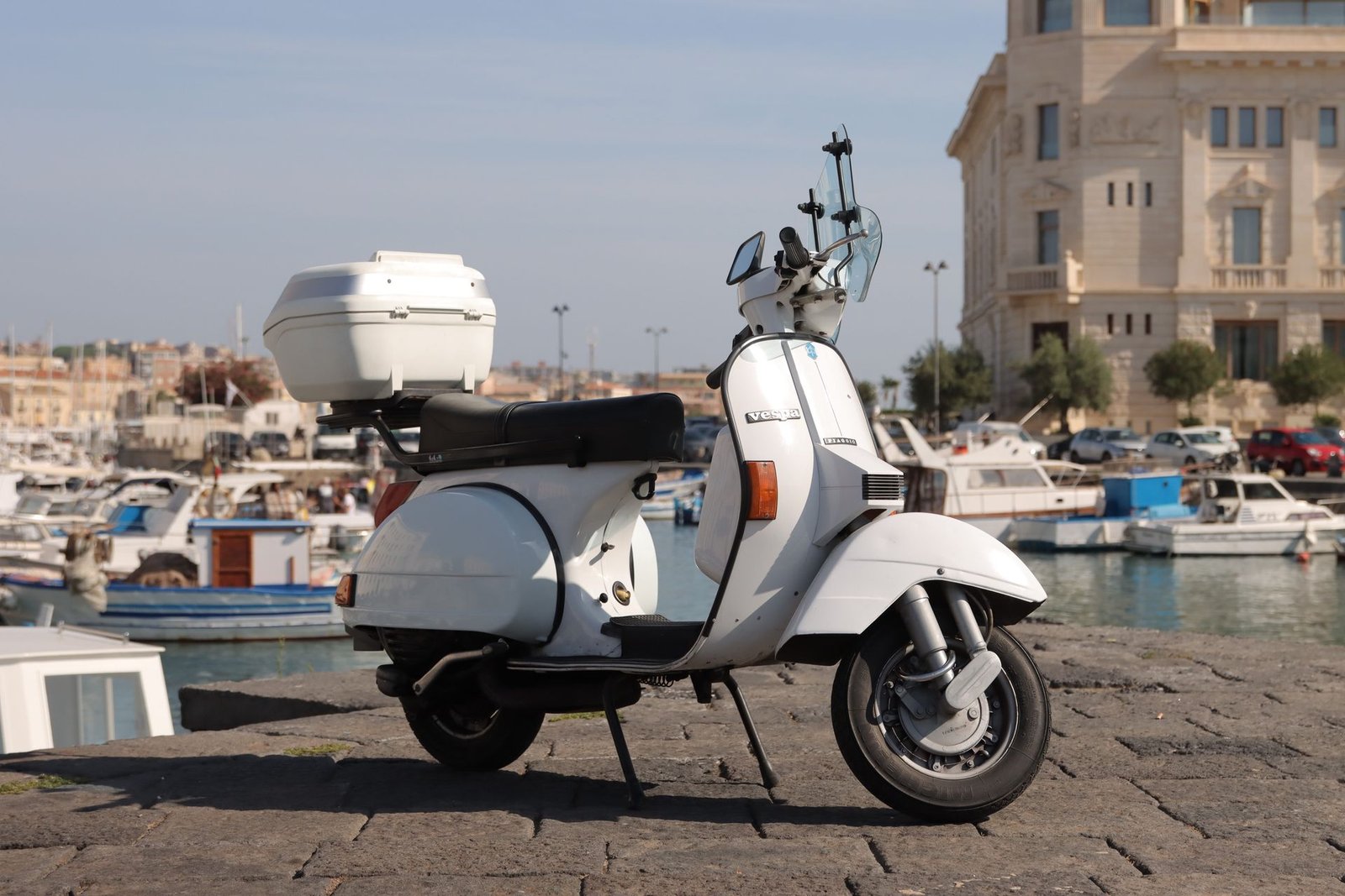 Scooter classique garée dans un petit port méditerranéen avec des barques, comme celui de La Savina à Formentera